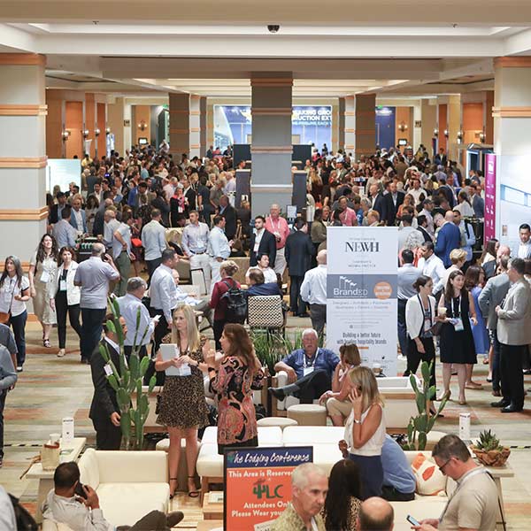 A large crowd of attendees networking and visiting exhibitor booths in a busy conference hall during The Lodging Conference.